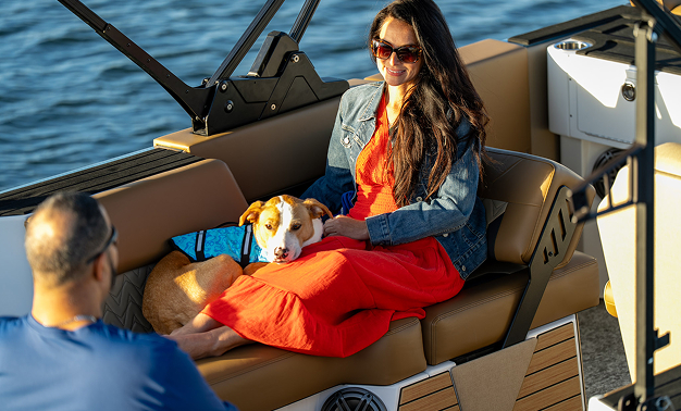 A woman and her dog sit together on the back of a boat, enjoying the view and the fresh air.